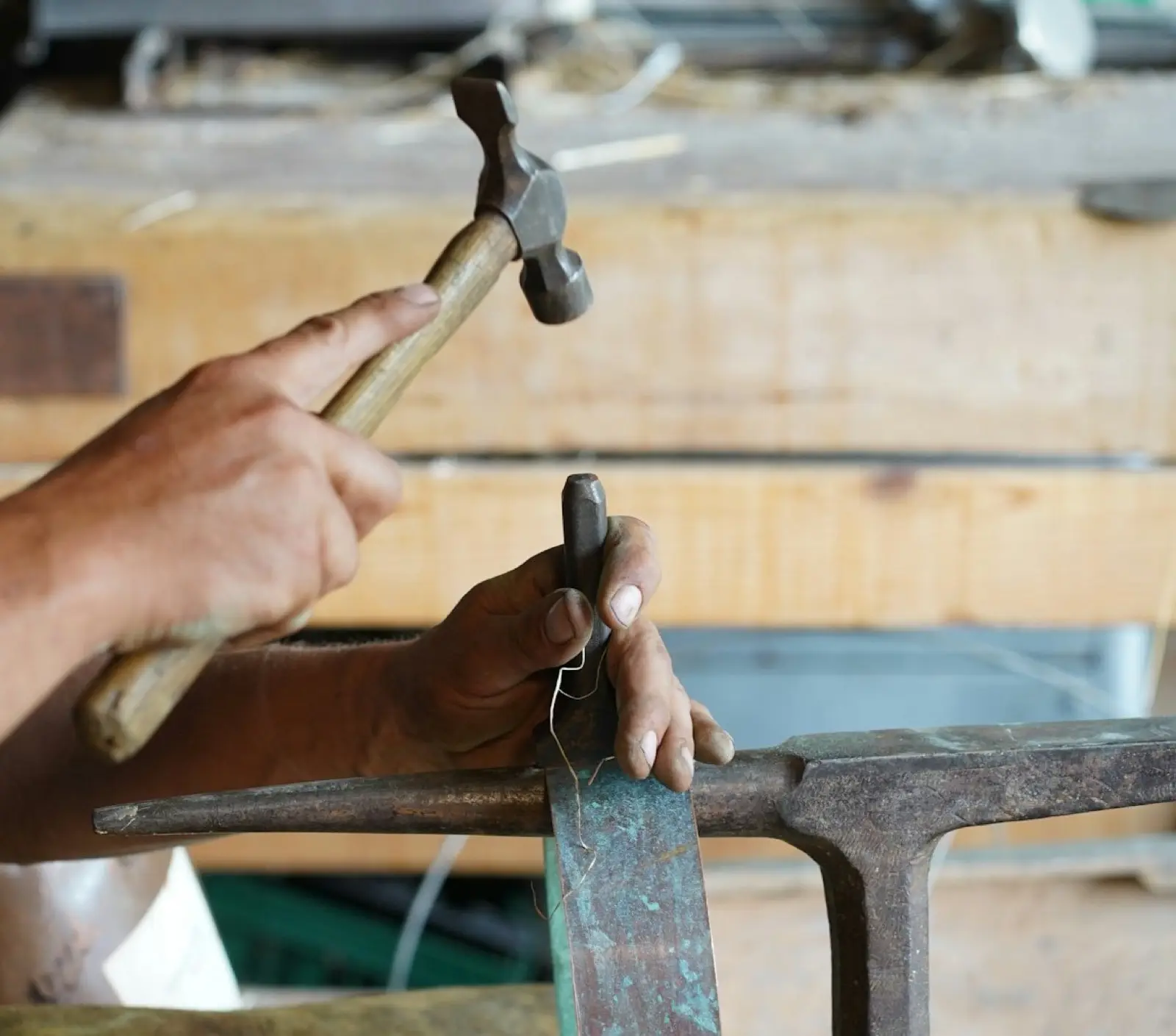 Hände treiben mit einem Hammer ein Kupferblech über einem Amboss