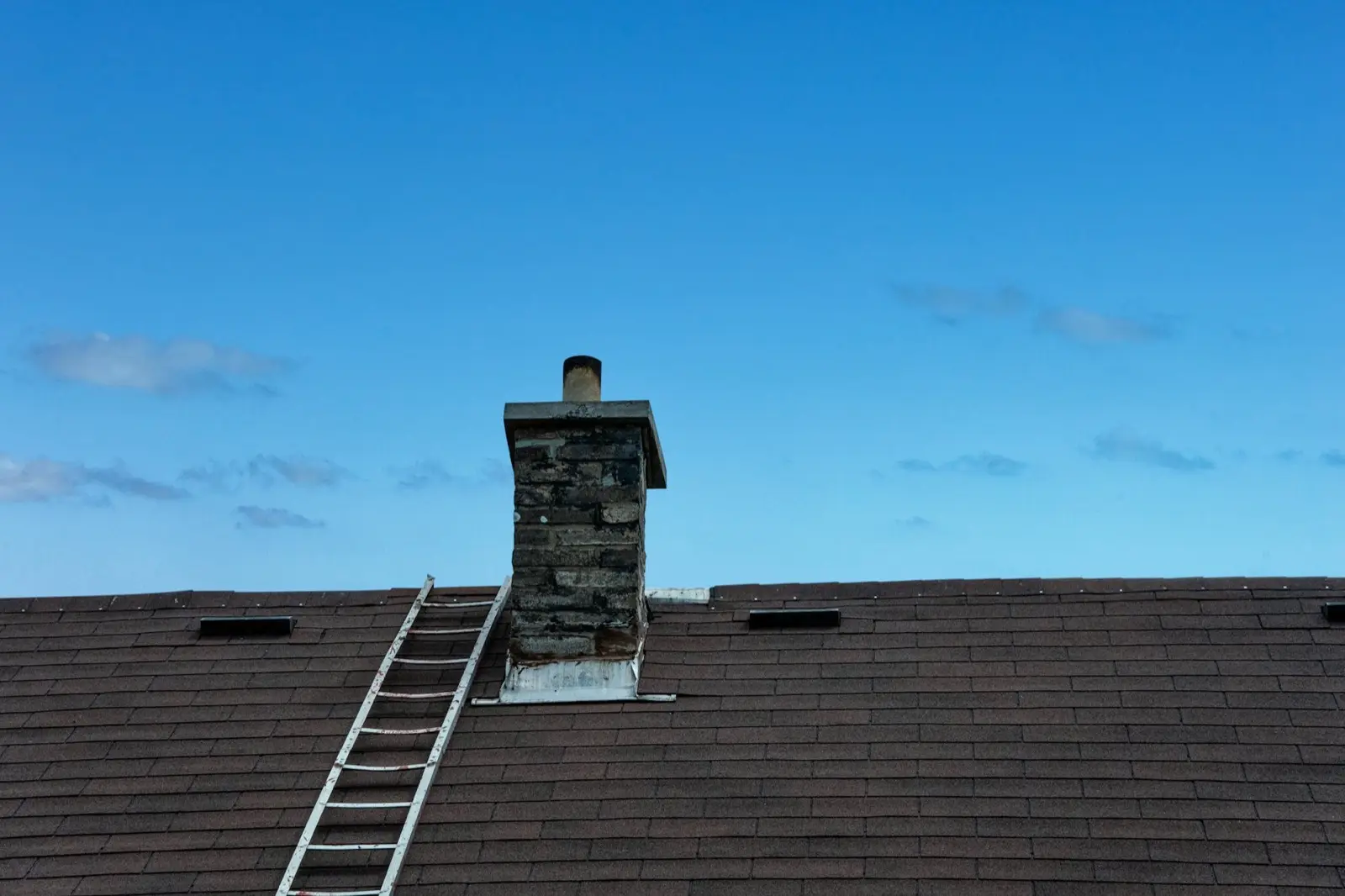 Gemauerter Kamin auf einem Dach, daneben eine Leiter